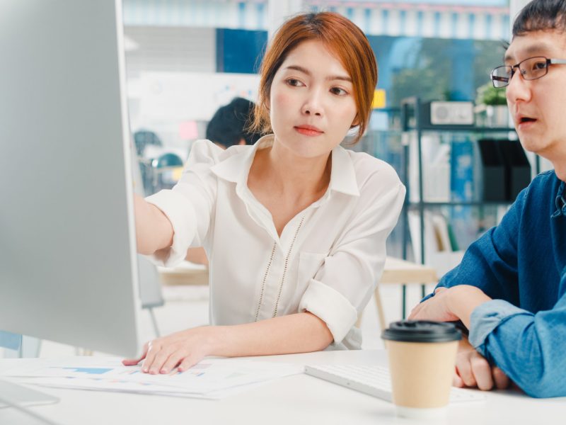 Millennial group of young Asia businessman and businesswoman in small modern urban office. Japanese male boss supervisor teaching intern or new employee korean girl helping with difficult assignment.